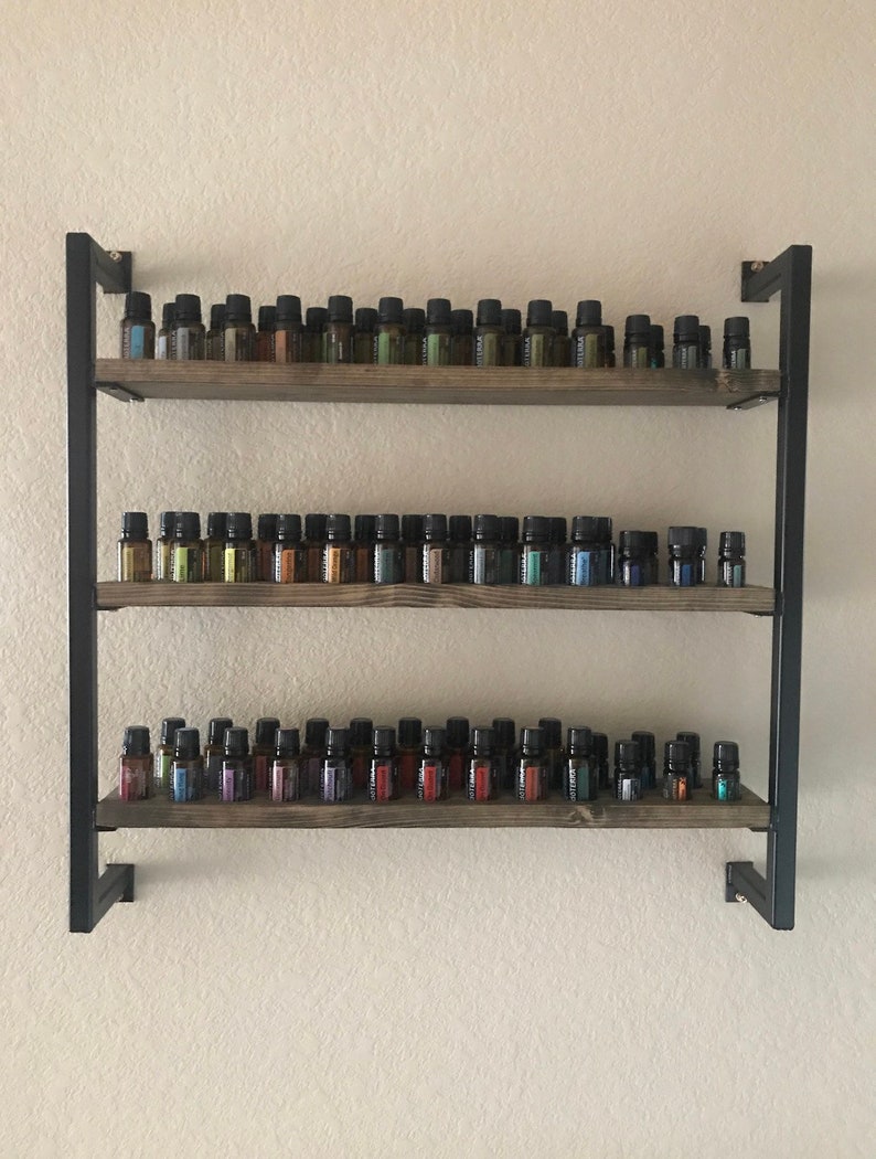May include: A three-tiered wooden shelf unit with black metal framing. The shelves are filled with rows of small glass bottles, each with a different colored liquid inside.