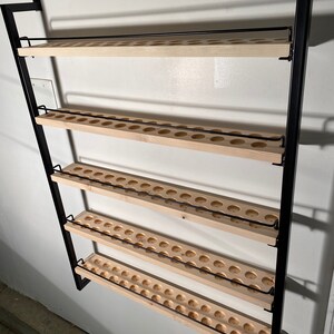May include: A black metal wall-mounted shelf with four wooden shelves. Each shelf has a row of evenly spaced circular holes.
