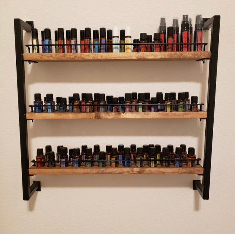May include: A black metal shelf unit with three wooden shelves, filled with small glass bottles of essential oils. The bottles are arranged in rows and are of various colors.