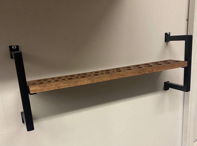 May include: A wooden shelf with a black metal frame. The shelf has a series of round holes drilled into the surface. The shelf is mounted to a wall.