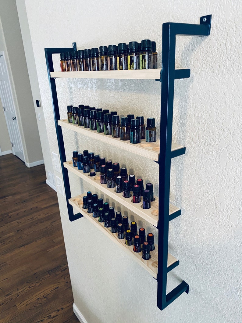 May include: A black metal wall-mounted shelf with four wooden shelves, each holding rows of small glass bottles. The bottles are filled with colorful liquids.