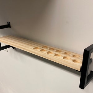 May include: A wooden shelf with black metal brackets. The shelf has 15 round cutouts for holding items.