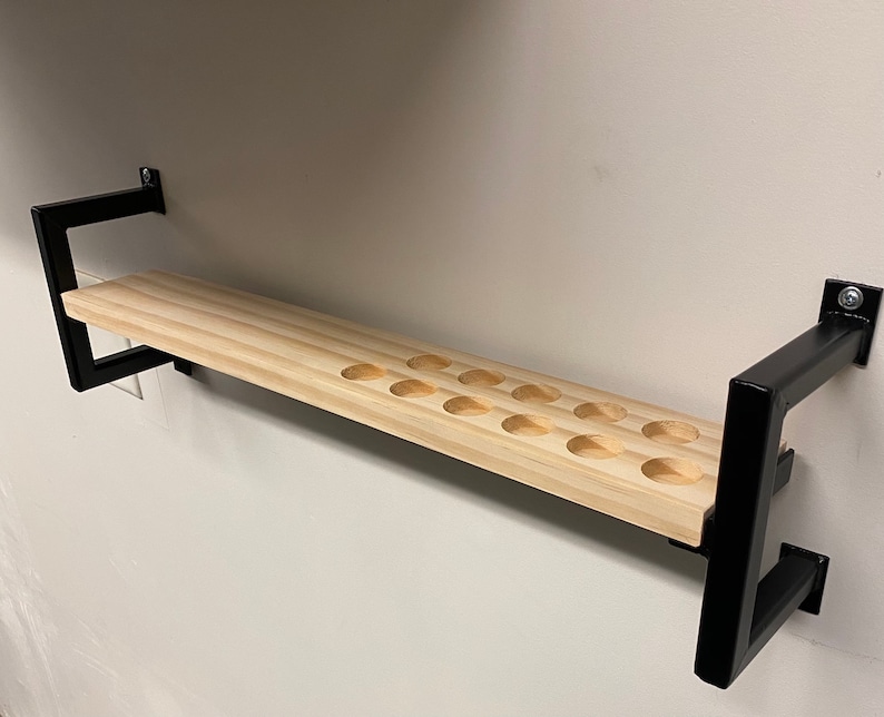 May include: A wooden shelf with black metal brackets. The shelf has 15 round cutouts for holding items.