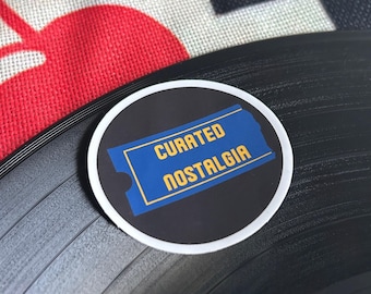 May include: A black vinyl record with a white sticker that says "Curated Nostalgia" in blue and yellow text.