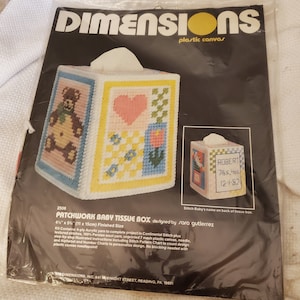 May include: A plastic canvas kit for a patchwork baby tissue box. The kit includes yarn, needle, and instructions. The finished size is 4 1/2 inches by 5 1/2 inches (11 cm by 15 cm). The design features a teddy bear, a heart, flowers, and a tulip.