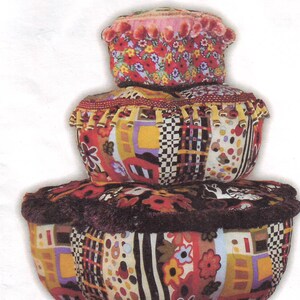May include: Three colorful fabric storage boxes with floral and geometric patterns. The top box has a pink pom-pom trim. The middle box has a brown beaded trim. The bottom box has a brown fringe trim.