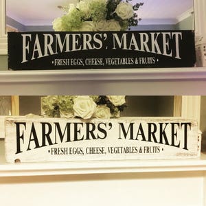 Peut inclure: Deux enseignes en bois avec des lettres noires et blanches qui indiquent "FARMERS' MARKET" avec le slogan "FRESH EGGS, CHEESE, VEGETABLES & FRUITS".
