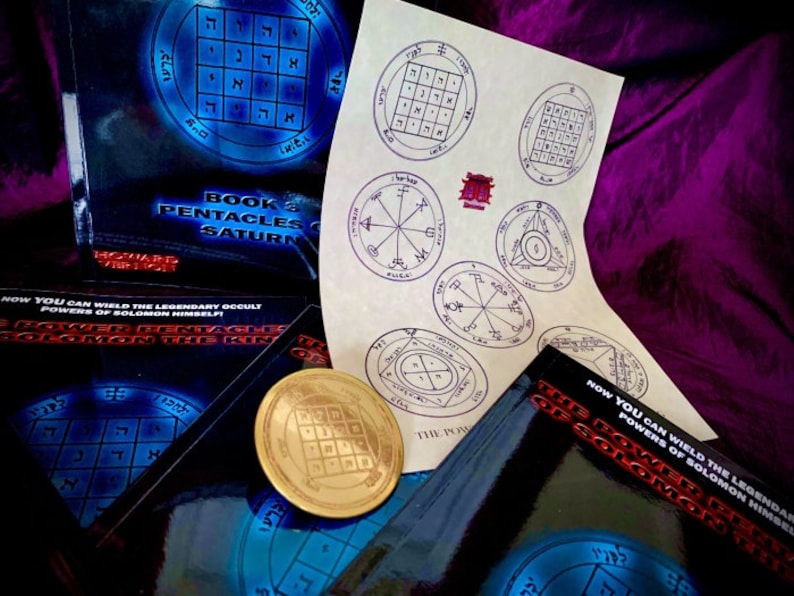 May include: A collection of books and a gold-colored metal disc with a pentagram design. The books are titled "Book 3 Pentacles of Saturn" and "The Power of Solomon the King". The books have a black background with blue and white text. The disc is on a black surface.