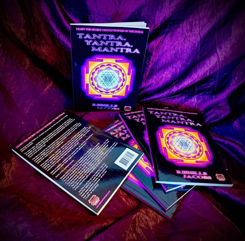 Op de afbeelding: Een stapel van vijf paperback boeken met een zwarte omslag en gouden letters. De titel van het boek is "TANTRA. YANTRA. MANTRA. LEARN THE SECRET OCCULT POWERS OF THE INDIANS" met een kleurrijk geometrisch ontwerp op de voorkant. De auteur is "REBEILLE JACOBS".