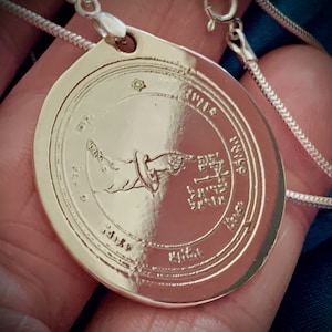 May include: Silver pendant necklace with a circular charm featuring an angel with wings and Hebrew text. The charm is surrounded by a circle of Hebrew text.