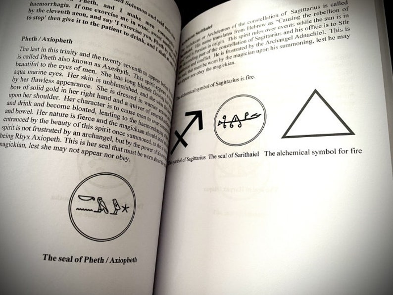 May include: A book page with black and white illustrations of symbols. The text on the page reads "The seal of Sarithaiel The alchemical symbol for fire".