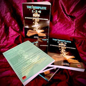 May include: A stack of three black and gold books titled "The Complete 1-2-3 Book of Practical Holistic Transformational Magic" by James Flie and Duncan Collins. The books are on a red velvet surface.