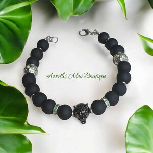 May include: Black beaded bracelet with a wolf head charm and green crystal accents. The bracelet has a silver clasp.