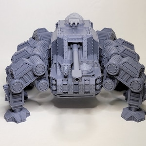 May include: A gray, detailed, plastic model of a six-legged tank with a large cannon on the front. The tank has a turret on top with two smaller cannons.