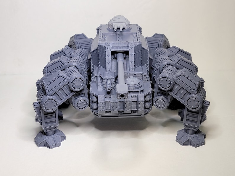 May include: A gray, detailed, plastic model of a six-legged tank with a large cannon on the front. The tank has a turret on top with two smaller cannons.