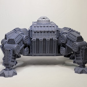 May include: A gray, detailed, 3D printed model of a four-legged, mechanical walker with a large, rectangular body and a small, round turret on top.