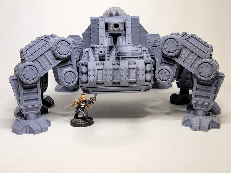May include: A gray, detailed, articulated, multi-legged, mechanical walker with a large cannon on top. A small, painted, plastic figure of a soldier stands in front of the walker.