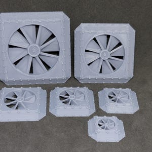May include: A collection of gray, 3D-printed fan models in various sizes. Each model features a central fan blade design within a square or octagonal frame, with small, rounded details around the edges. The models are arranged on a neutral surface.