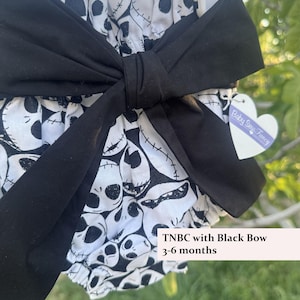 May include: A baby outfit with a black bow. The outfit is white with a black skull pattern. The text "TNBC with Black Bow 3-6 months" is visible. A heart-shaped tag with the text "Baby Sew Fancy" is attached.
