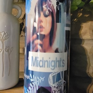 Puede incluir: Un vaso azul y morado con un collage de im&aacute;genes, incluyendo una mujer con una estrella en la frente, una nota musical, una rama con hojas y una caja de m&uacute;sica de estilo vintage. El texto "Lavender Haze" y "Midnights" est&aacute; impreso en el vaso.
