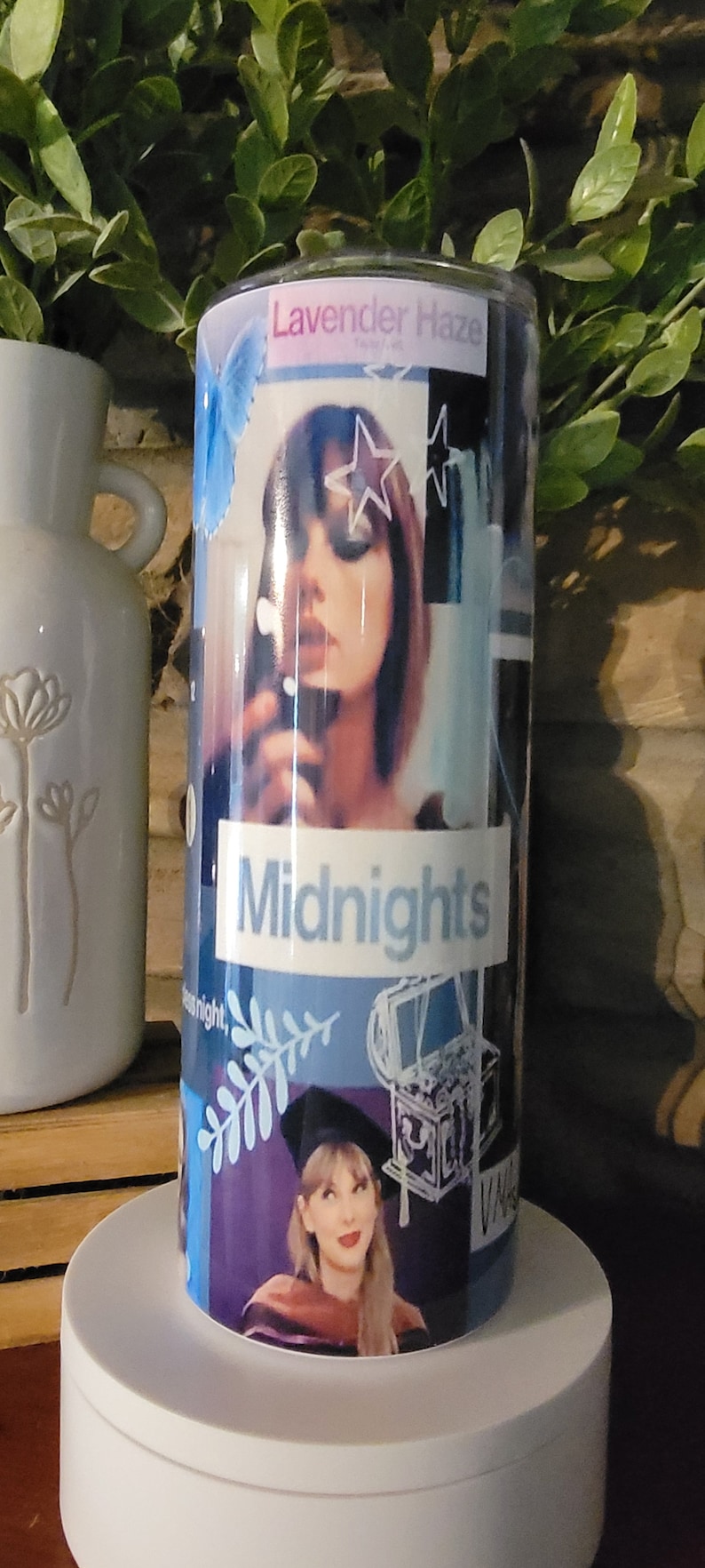 Puede incluir: Un vaso azul y morado con un collage de im&aacute;genes, incluyendo una mujer con una estrella en la frente, una nota musical, una rama con hojas y una caja de m&uacute;sica de estilo vintage. El texto "Lavender Haze" y "Midnights" est&aacute; impreso en el vaso.