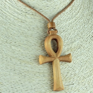 May include: A wooden Ankh pendant necklace with a brown leather cord. The Ankh is a symbol of life in ancient Egyptian culture.