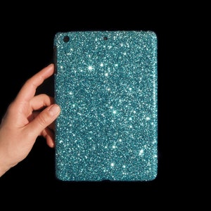 May include: A teal glitter tablet case. The case is rectangular with rounded corners and a sparkling, textured surface. The case is held against a black background.