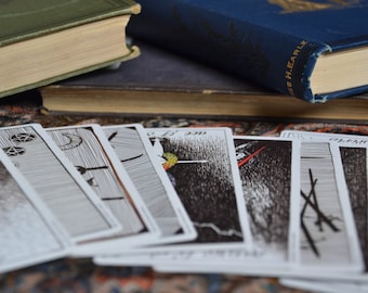 Puede incluir: Un conjunto de cartas de tarot extendidas sobre una alfombra con estampado. Las cartas están boca arriba y muestran ilustraciones en blanco y negro. Las cartas están dispuestas en forma de abanico.