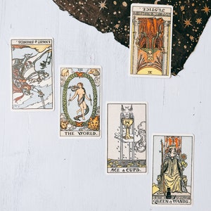 Può includere: Carte dei tarocchi disposte su una superficie di legno bianco. Le carte sono: Cavaliere di Spade, Il Mondo, Asso di Coppe, Regina di Bacchette e Giustizia.