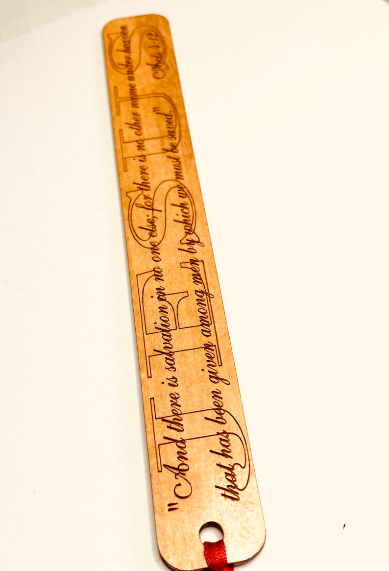 May include: A wooden bookmark with a red ribbon. The bookmark has the text "And there is salvation in no one else; for there is no other name under heaven by which we must be saved." Acts 4:12