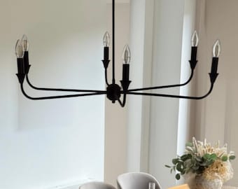 Puede incluir: Una lámpara de araña de metal negro mate con seis bombillas tipo vela suspendida sobre una mesa de comedor rectangular de madera. La mesa está rodeada por seis sillas tapizadas en gris y cuenta con manteles individuales redondos y un centro floral.