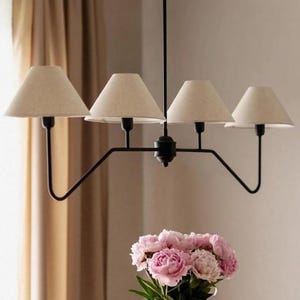 May include: A black metal chandelier with four beige fabric shades. The light fixture has a central stem and curved arms. A bouquet of pink flowers sits below the chandelier, adding a touch of colour to the neutral tones.