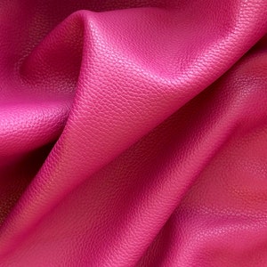May include: Close-up of a textured, pink leather fabric. The fabric is folded and draped, showing the texture and color.