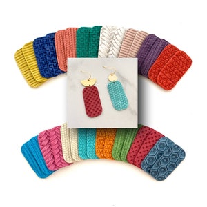 May include: A pair of dangle earrings with geometric shapes. The earrings are made of red and blue leather with gold accents. The earrings are displayed on a white surface with a variety of colorful leather swatches in the background.