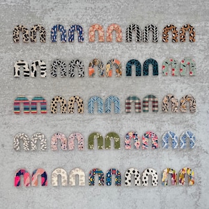May include: A set of 20 pairs of colourful arch-shaped earrings with various patterns. The earrings are made of wood and have a natural finish.