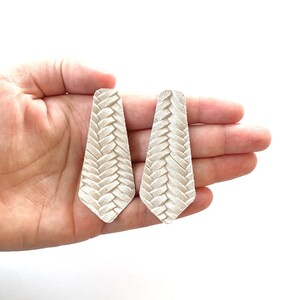 Puede incluir: Un par de pendientes de cuero blanco con un dise&ntilde;o trenzado.