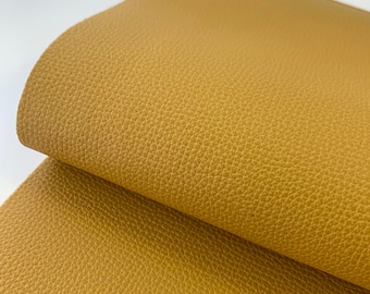 May include: A close-up of a piece of mustard yellow faux leather fabric. The fabric has a textured surface that resembles leather.