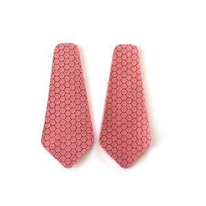 Puede incluir: Un par de pendientes de cuero rosa con un patr&oacute;n hexagonal. Los pendientes tienen forma de l&aacute;grima.