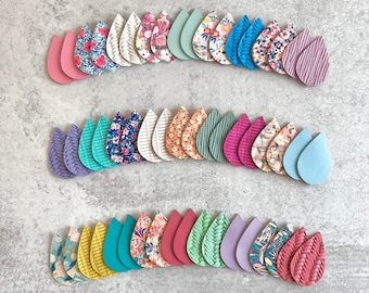 Op de afbeelding: Een verzameling druppelvormige oorbellen in verschillende kleuren en patronen. De oorbellen bevatten effen kleuren zoals roze, blauw en groen, evenals bloemen-, gestreepte en textuurontwerpen. De oorbellen zijn in drie rijen gerangschikt.