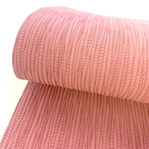 May include: Pink textured fabric with a ribbed pattern. The fabric is folded in half, showing the texture and pattern.