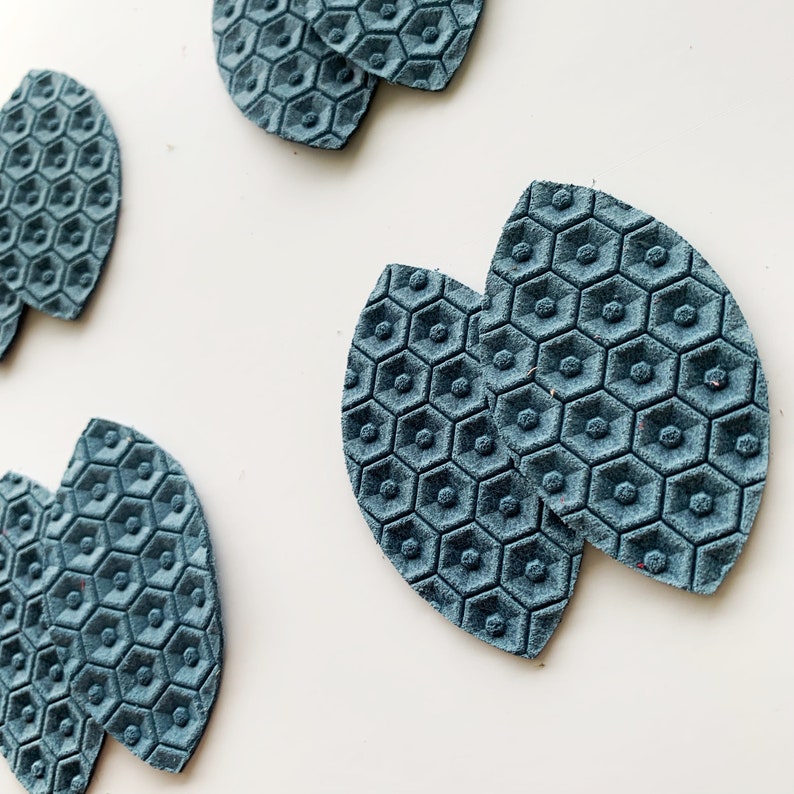 May include: Two teal blue leather earrings shaped like leaves with a honeycomb pattern.