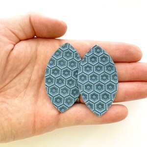 May include: A pair of blue leather earrings with a hexagonal pattern.