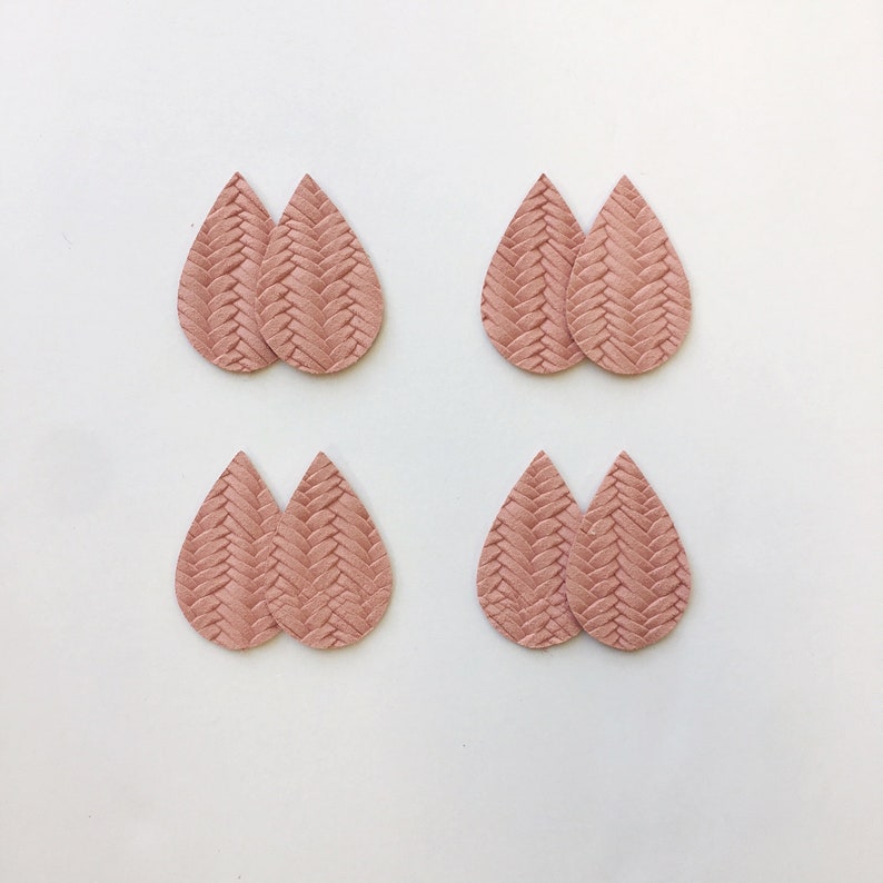 May include: Four pairs of teardrop earrings in a light rose hue. Each earring features a textured, woven design. The earrings are displayed against a white backdrop, highlighting their colour and pattern.