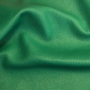 May include: Close-up of a textured green leather fabric. The leather has a pebbled surface and is folded in a soft, wavy pattern.