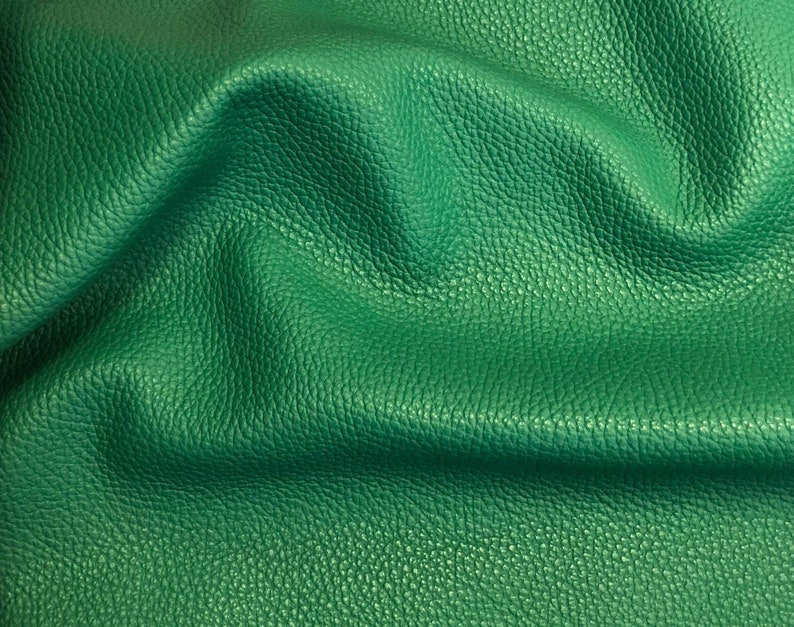 May include: Close-up of a textured green leather fabric. The leather has a pebbled surface and is folded in a soft, wavy pattern.