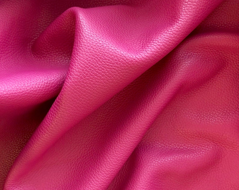 May include: Close-up of a textured, pink leather fabric. The fabric is folded and draped, showing the texture and color.