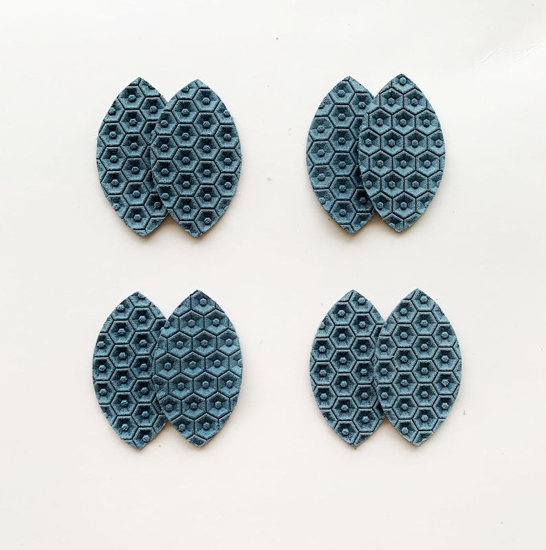 May include: Four pairs of teal blue faux leather earrings with a hexagonal pattern. The earrings are shaped like a leaf.