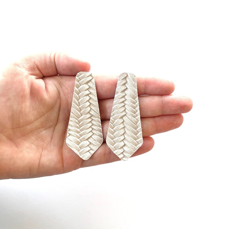 Puede incluir: Un par de pendientes de cuero blanco con un dise&ntilde;o trenzado.