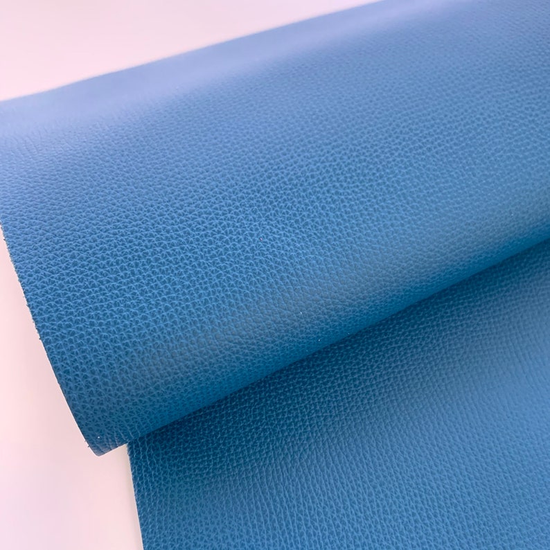 May include: A close-up of a blue textured faux leather fabric. The fabric has a pebbled texture and a slightly glossy finish.