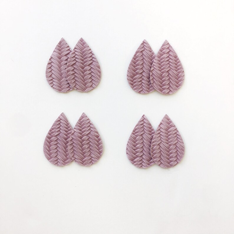 May include: Four pairs of mauve teardrop earrings with a woven texture are displayed against a white backdrop. The earrings are evenly spaced, highlighting their intricate design and colour.